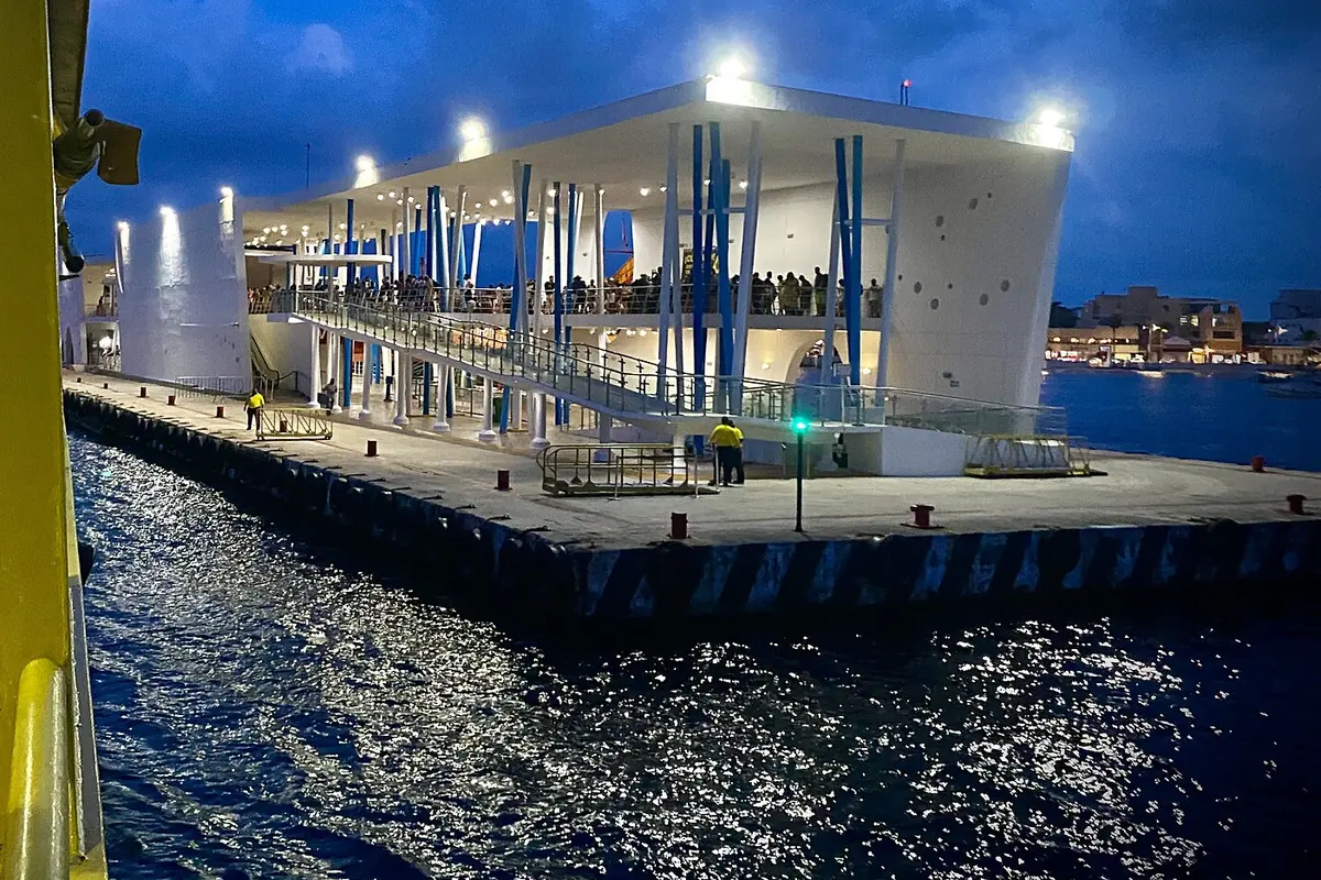 A lit white passenger ferry terminal on the water at dusk in San Miguel de Cozumel