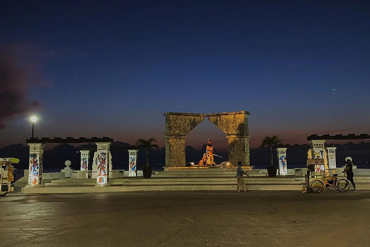 A stone arch and pillared gateway in San Miguel de Cozumel at night, lit by street lamps under a dark blue sky
