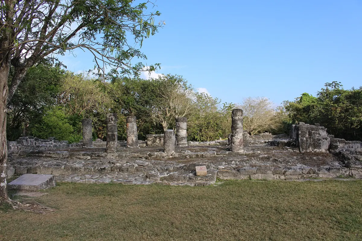 Low stone ruins with a row of short pillars in a clearing among tropical trees at San Gervasio on Cozumel